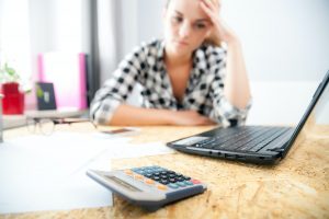 Stressed and depressed woman in home office calculating bills