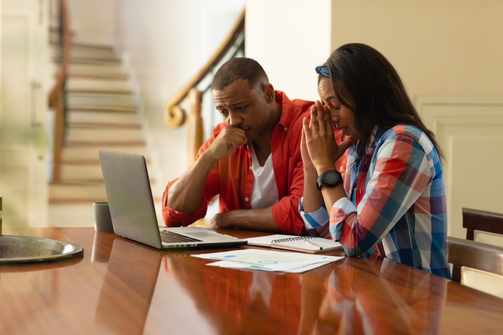 African american couple looking at laptop while sitting with financial bills at home